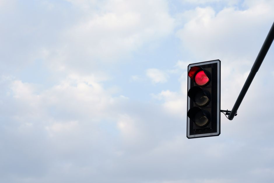 Red traffic light set against a bright, cloudy sky. Perfect for themes of travel, technology, and safety.