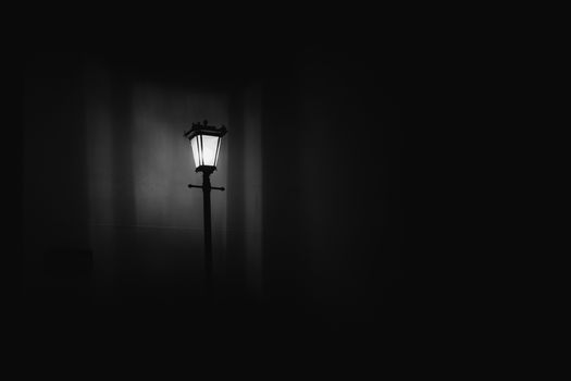 Captivating black and white photo of an illuminated street lamp against a dark background.