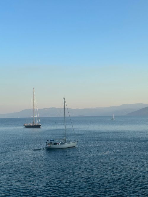 Free Peaceful scene of sailboats on calm ocean waters with distant hills during sunset. Stock Photo