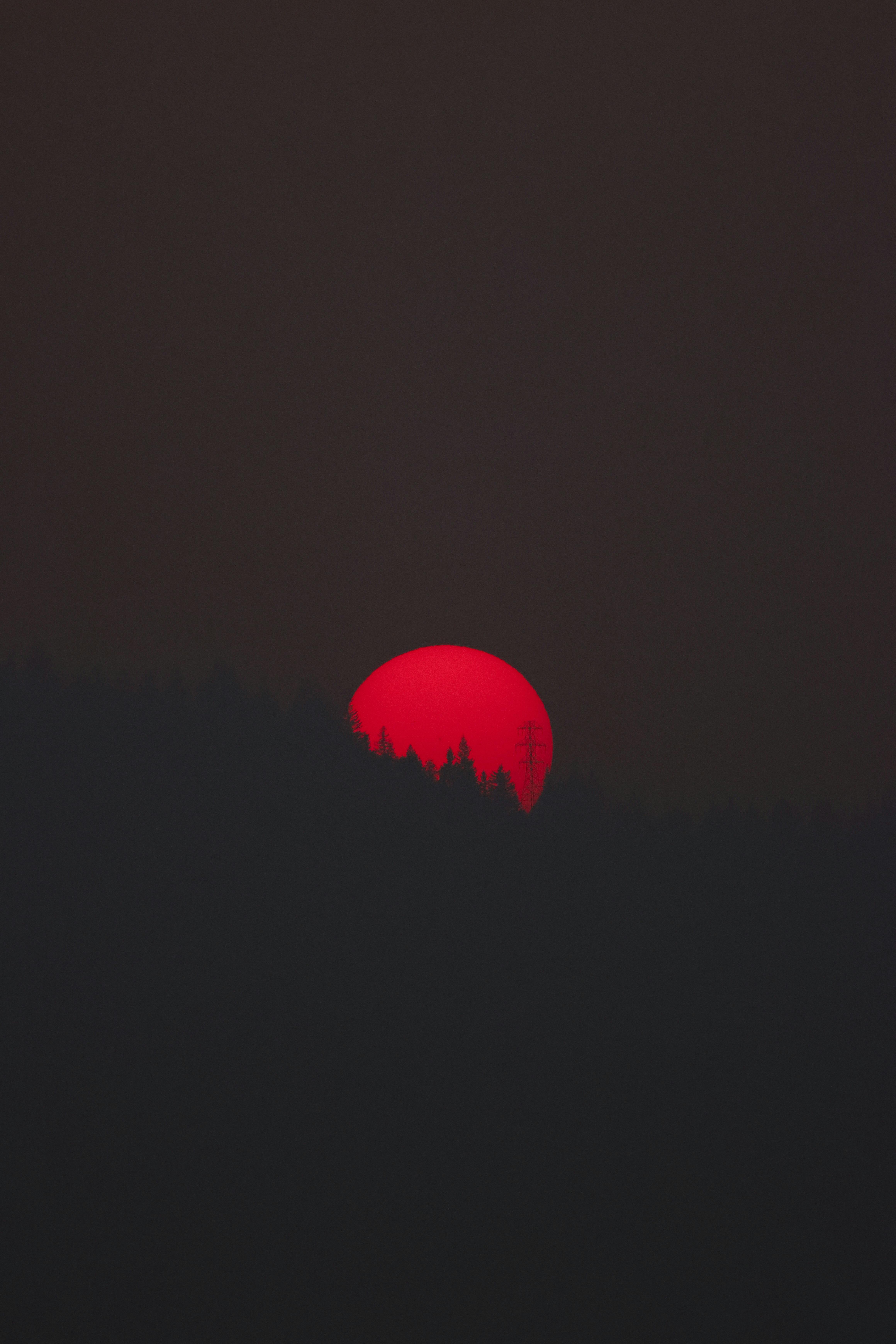 A striking red sun sets behind dark hills in Oregon, USA, creating a moody silhouette.