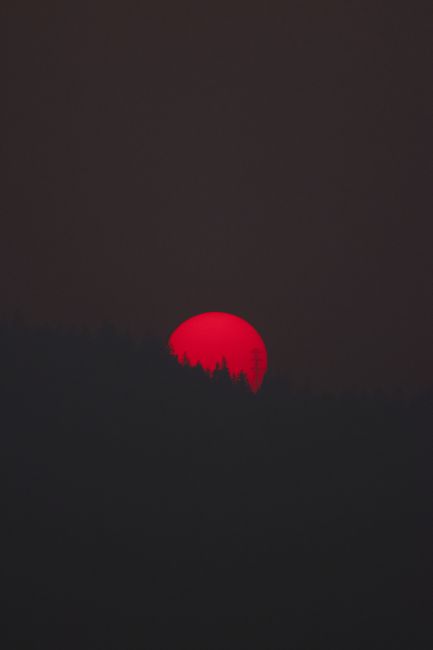 A striking red sun sets behind dark hills in Oregon, USA, creating a moody silhouette.