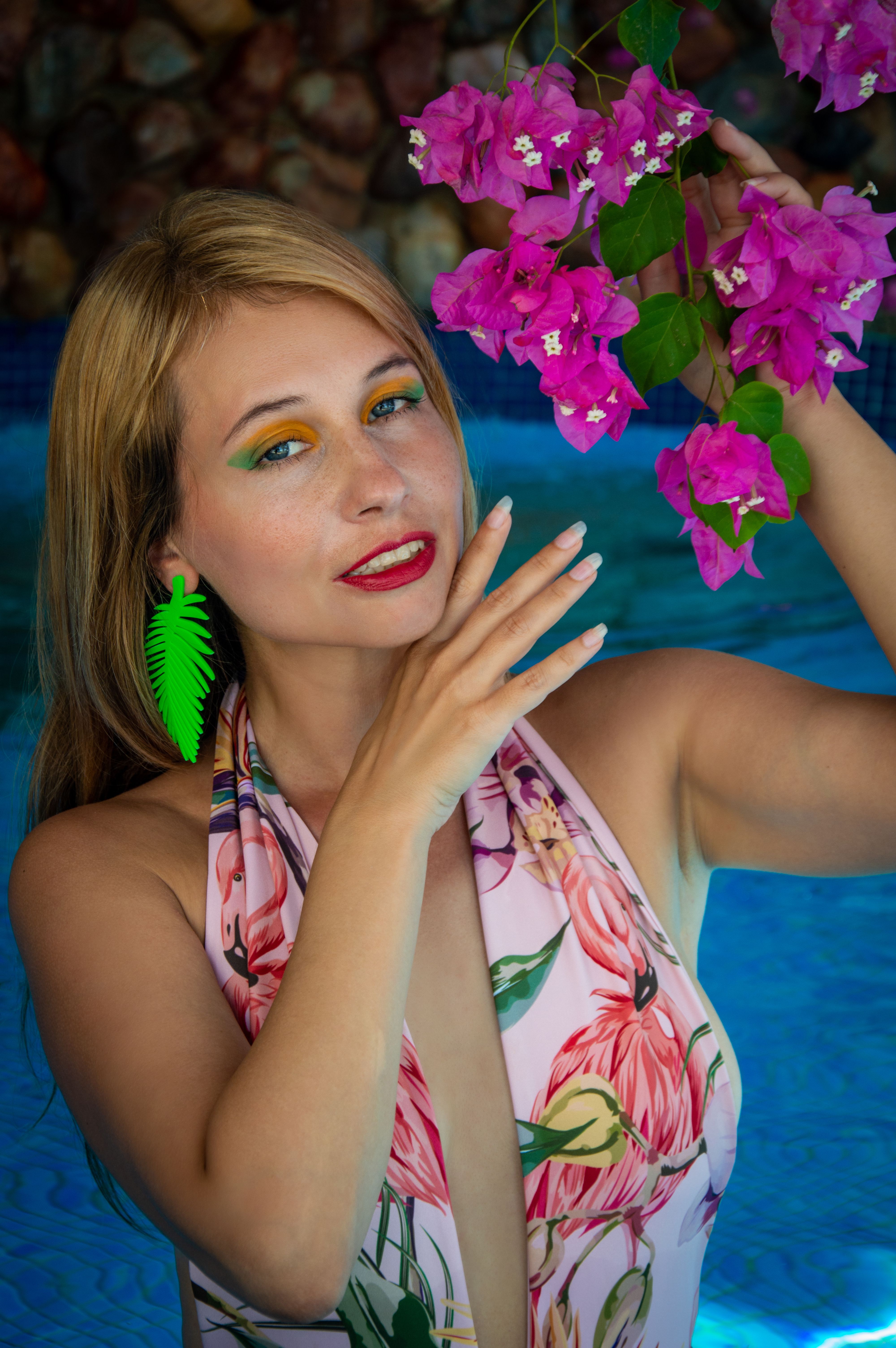 Vibrant summer portrait of a woman in floral print swimsuit holding bougainvillea.