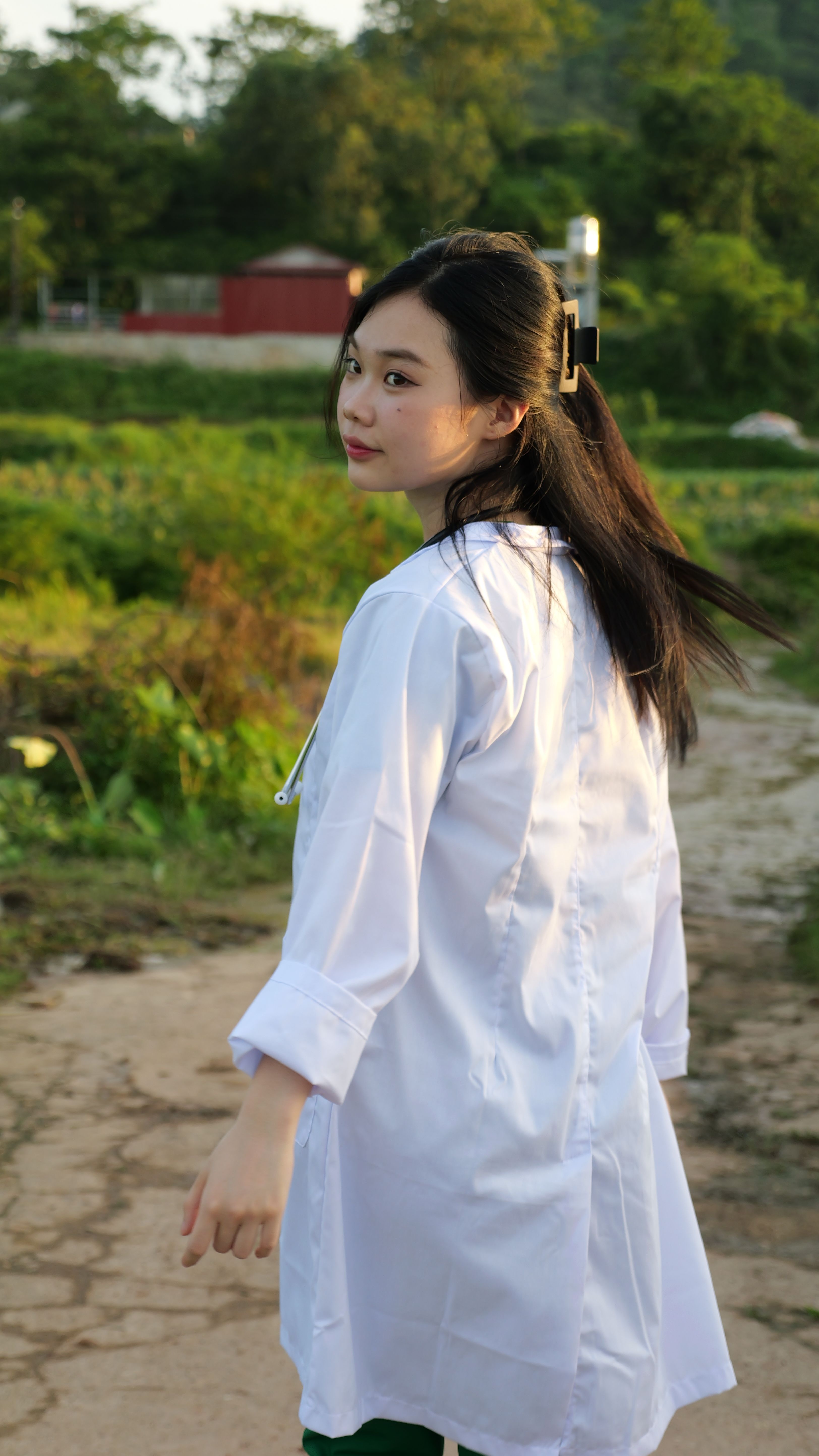 A young woman in a white coat walking outdoors in a serene summer landscape.