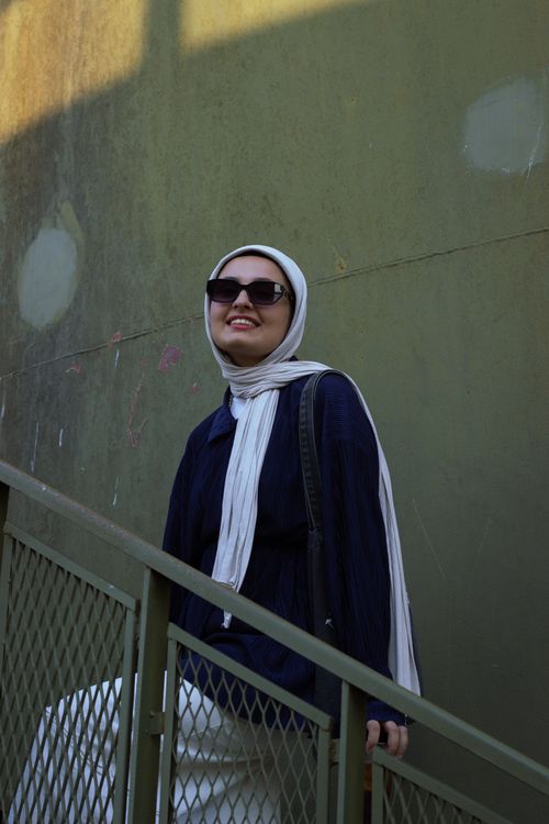Free Smiling woman in sunglasses and hijab poses confidently on an outdoor staircase. Stock Photo