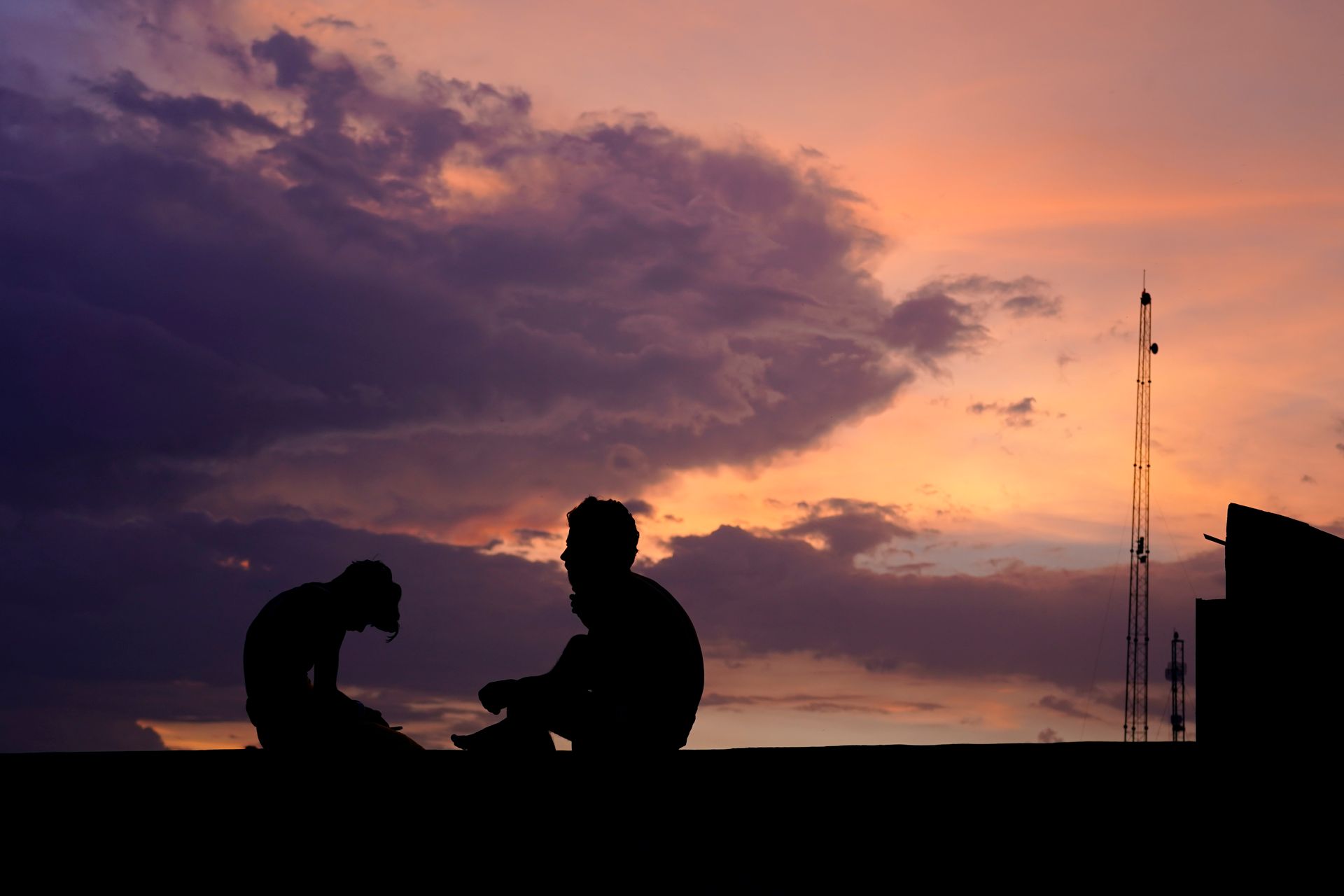 Silhouette of two people against a vivid sunset sky with dramatic clouds.