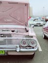 户外车展上，一辆粉色古董车敞着引擎盖的前视图