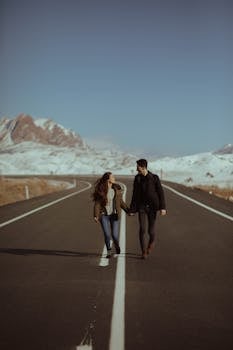 一对情侣手牵着手，走在风景优美的道路上，背景是雪山