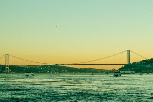 Free A suspension bridge spans a tranquil waterway at dusk with boats on the calm sea. Stock Photo