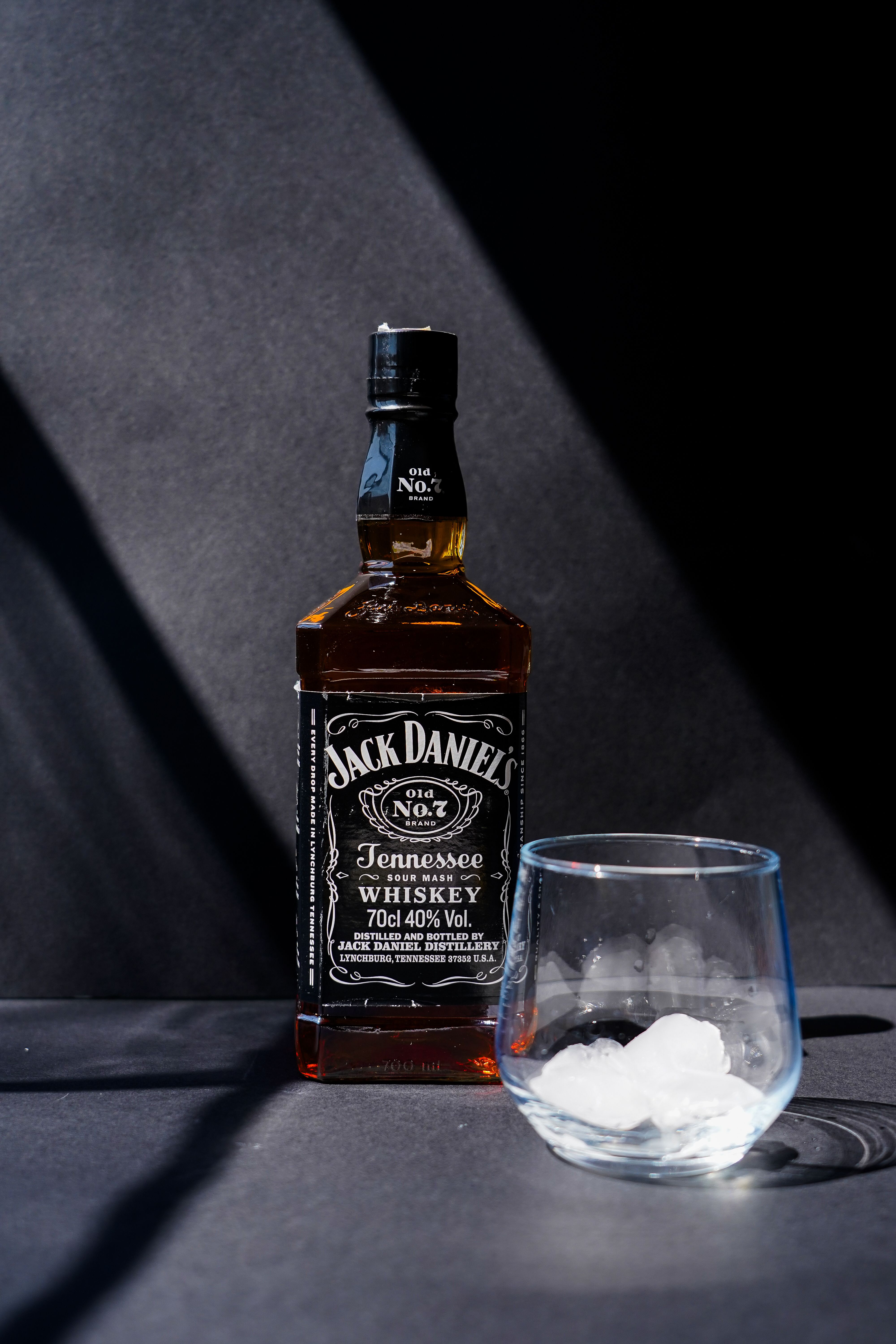 Jack Daniel's Tennessee Whiskey bottle with a glass of ice in dramatic lighting.