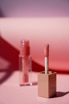 Close-up of a lip gloss applicator with a soft pink gradient background, ideal for beauty themes.