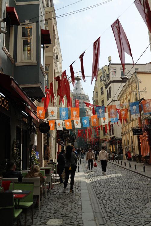 Free Colorful flags adorn a lively street near Istanbul's Galata Tower, bustling with locals and tourists. Stock Photo