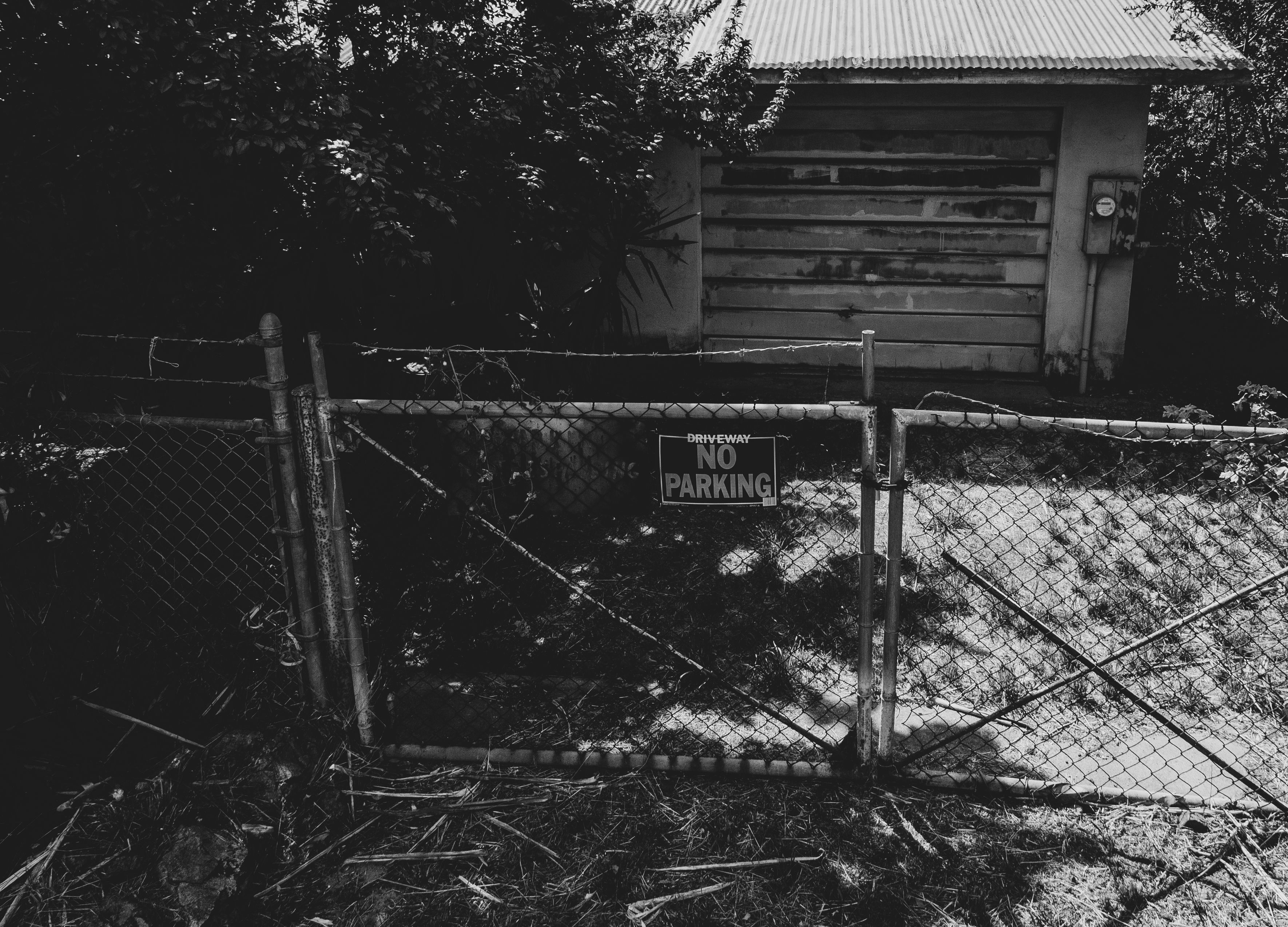 Gard din plasă de sârmă fotografiat alb-negru, cu o placă „No Parking” prinsă pe el