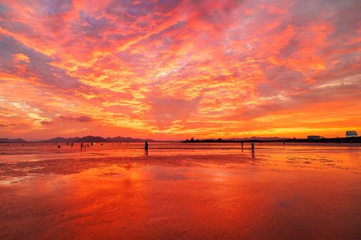 Stunning orange sunset reflecting over serene beach waters with silhouetted figures.