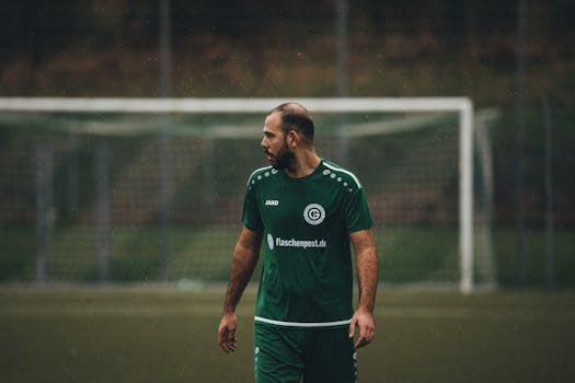 Soccer player in green uniform on a wet field during a rainy day match.