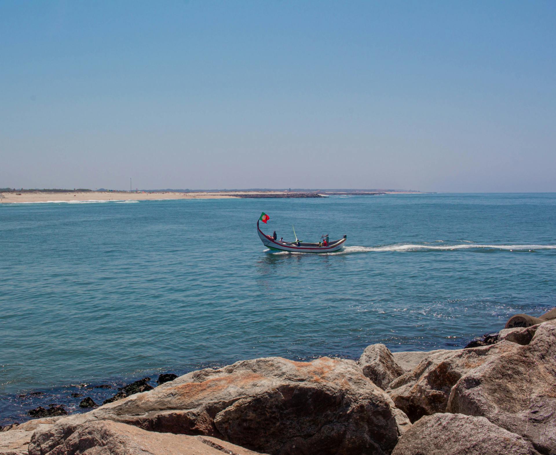 A traditional boat sails along the scenic rocky seashore on a bright summer day.