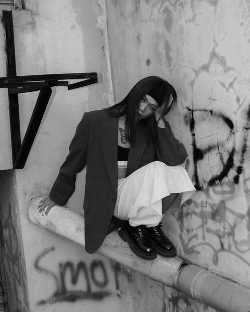 Free Black and white urban fashion portrait of a woman sitting against a graffiti-covered wall. Stock Photo