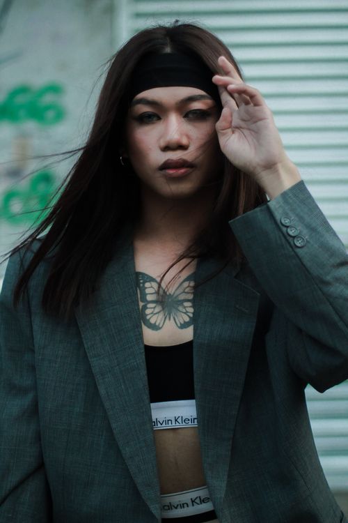Free Stylish young woman in a gray suit, showcasing a butterfly tattoo, posing confidently outdoors. Stock Photo