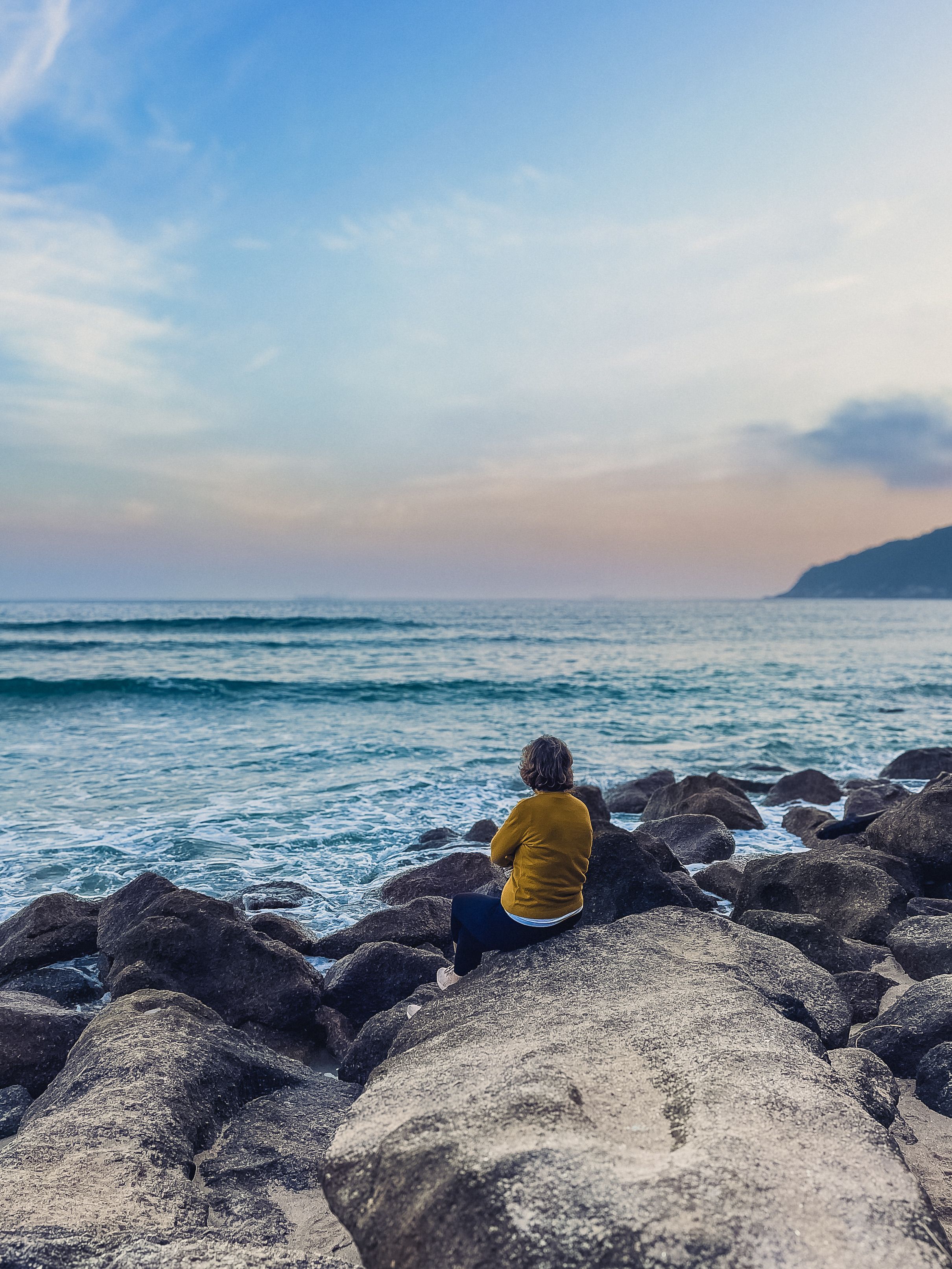 A person sitting on rocks looking out to the ocean · Free Stock Photo