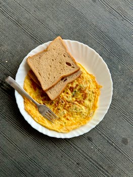 Top view of a toasted bread slice over an omelette on a white plate with a fork.