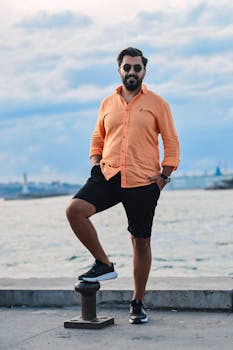 A confident man in sunglasses enjoying a sunny day by the seaside, striking a relaxed pose.