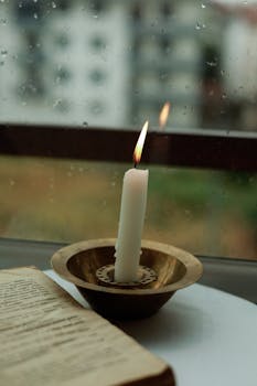 A solitary candle burning by a rainy window evokes warmth and tranquility.