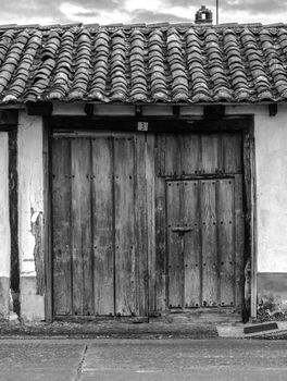 Monochrome image of an old rustic wooden door with a tiled roof.