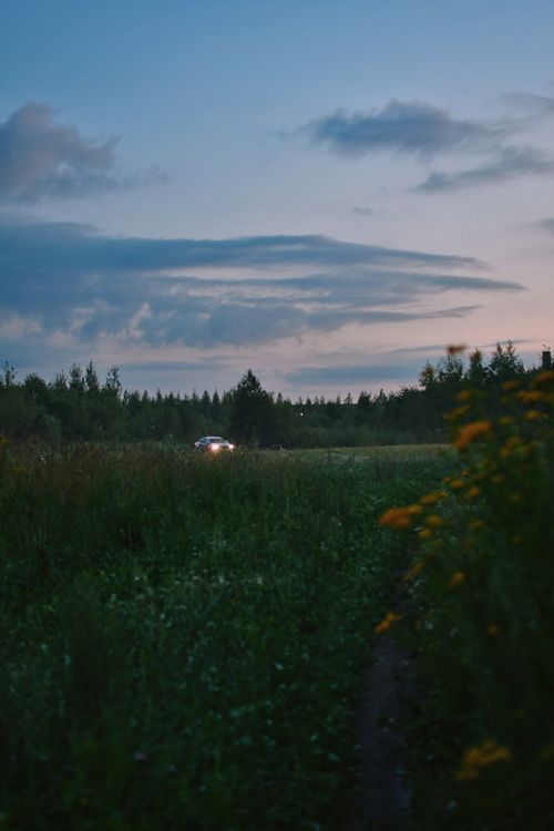 Free A tranquil evening scene with a car in a meadow under a colorful sky. Stock Photo