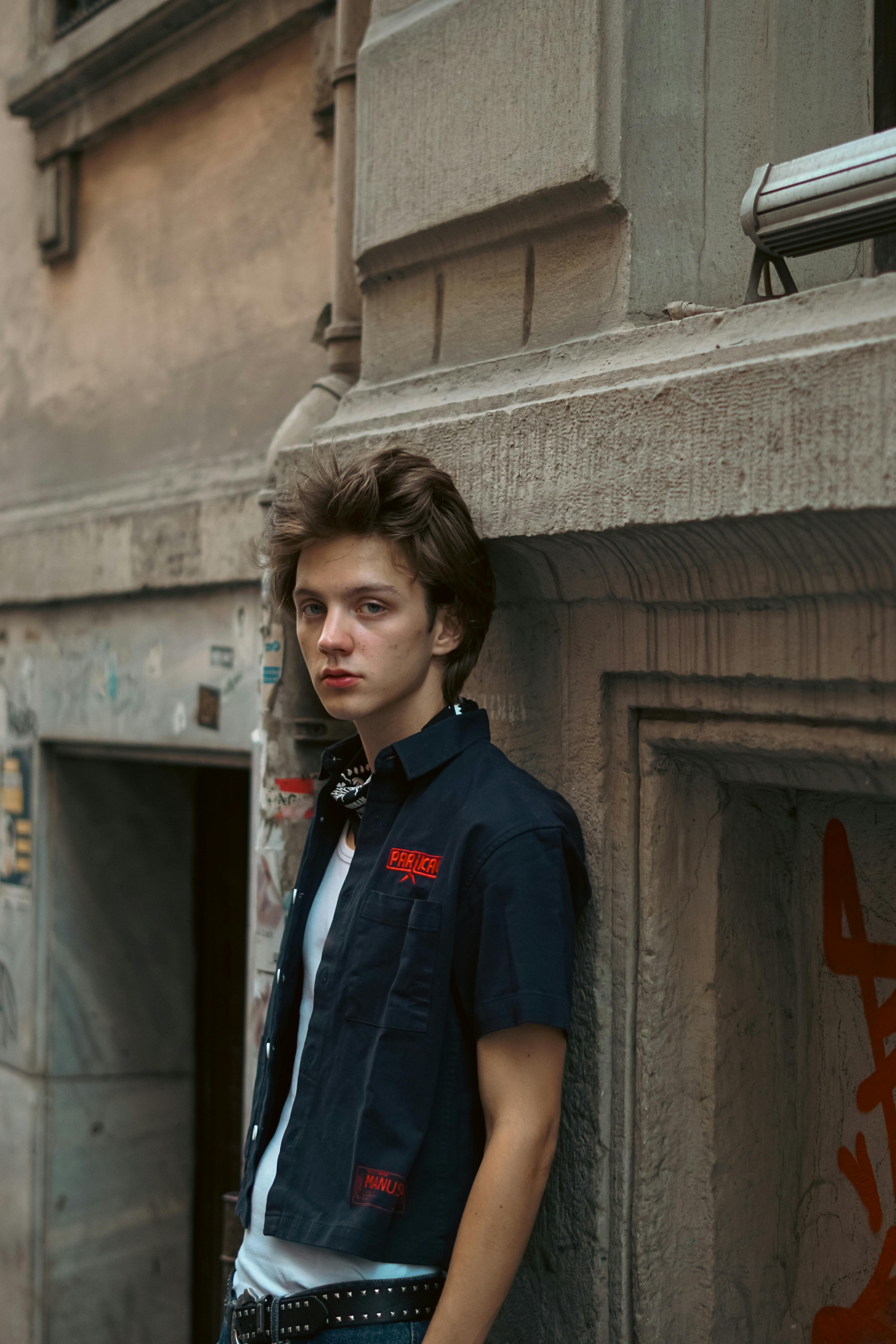 a young man leaning against a wall with a guitar