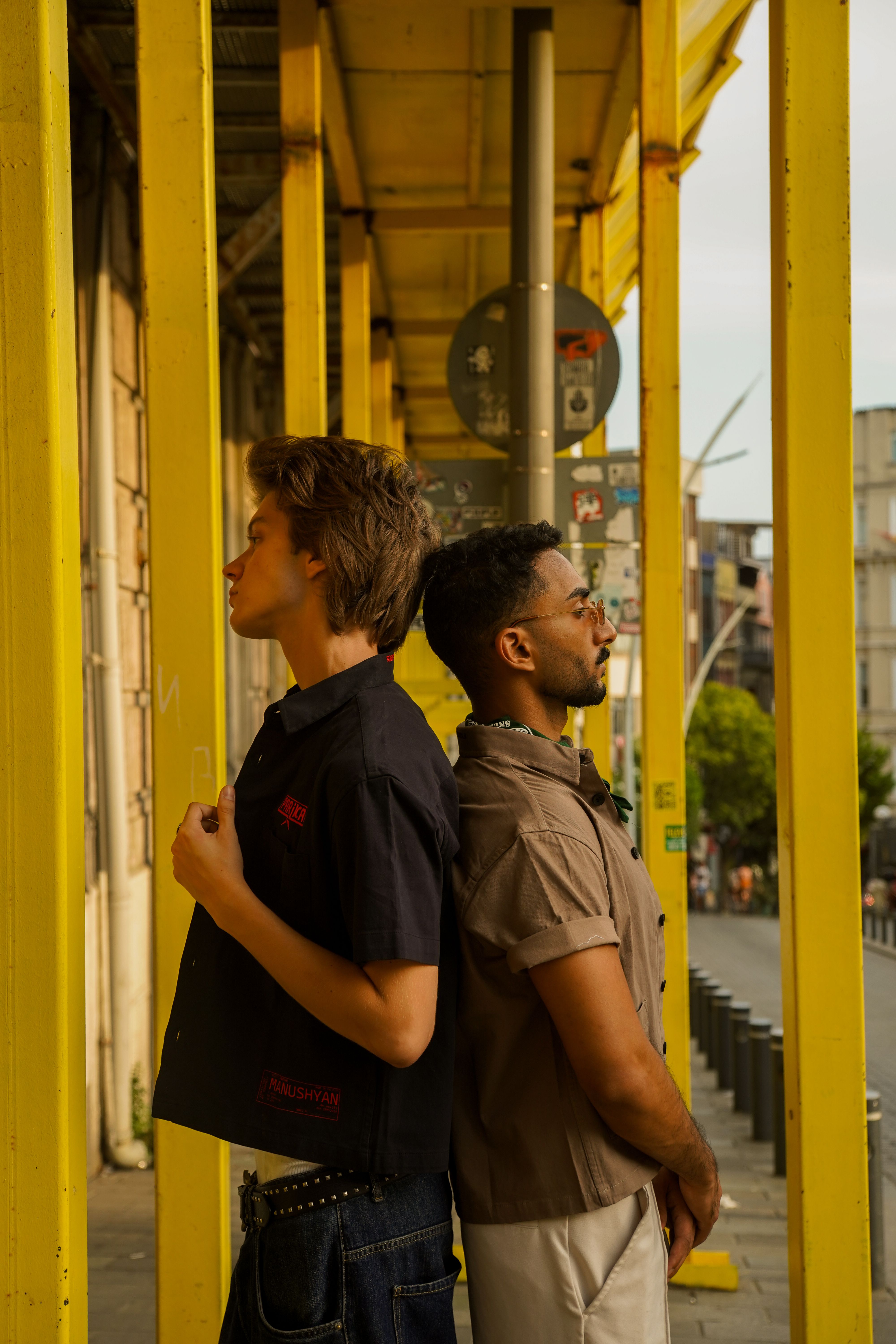 Two men standing next to each other in front of a yellow building ...
