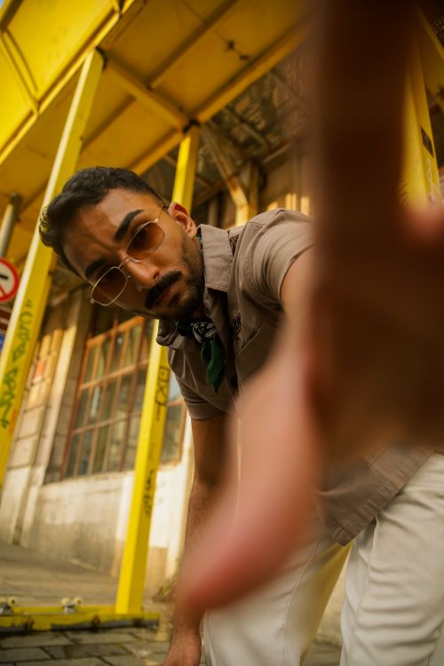 Free Portrait of a young man in sunglasses reaching towards the camera outdoors against urban and industrial background. Stock Photo