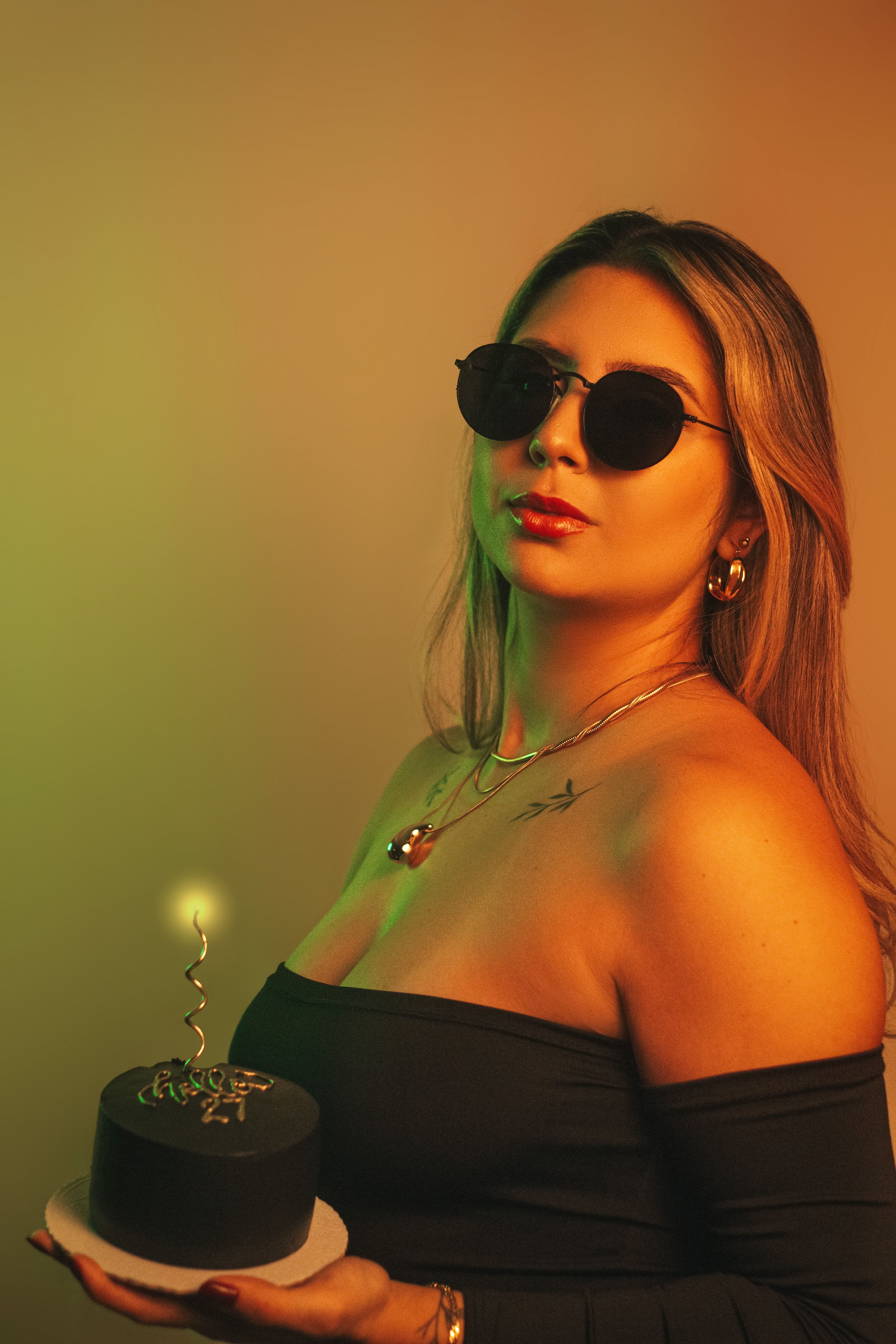 A fashionable woman holding a cake with a candle, wearing sunglasses in a retro ambiance.