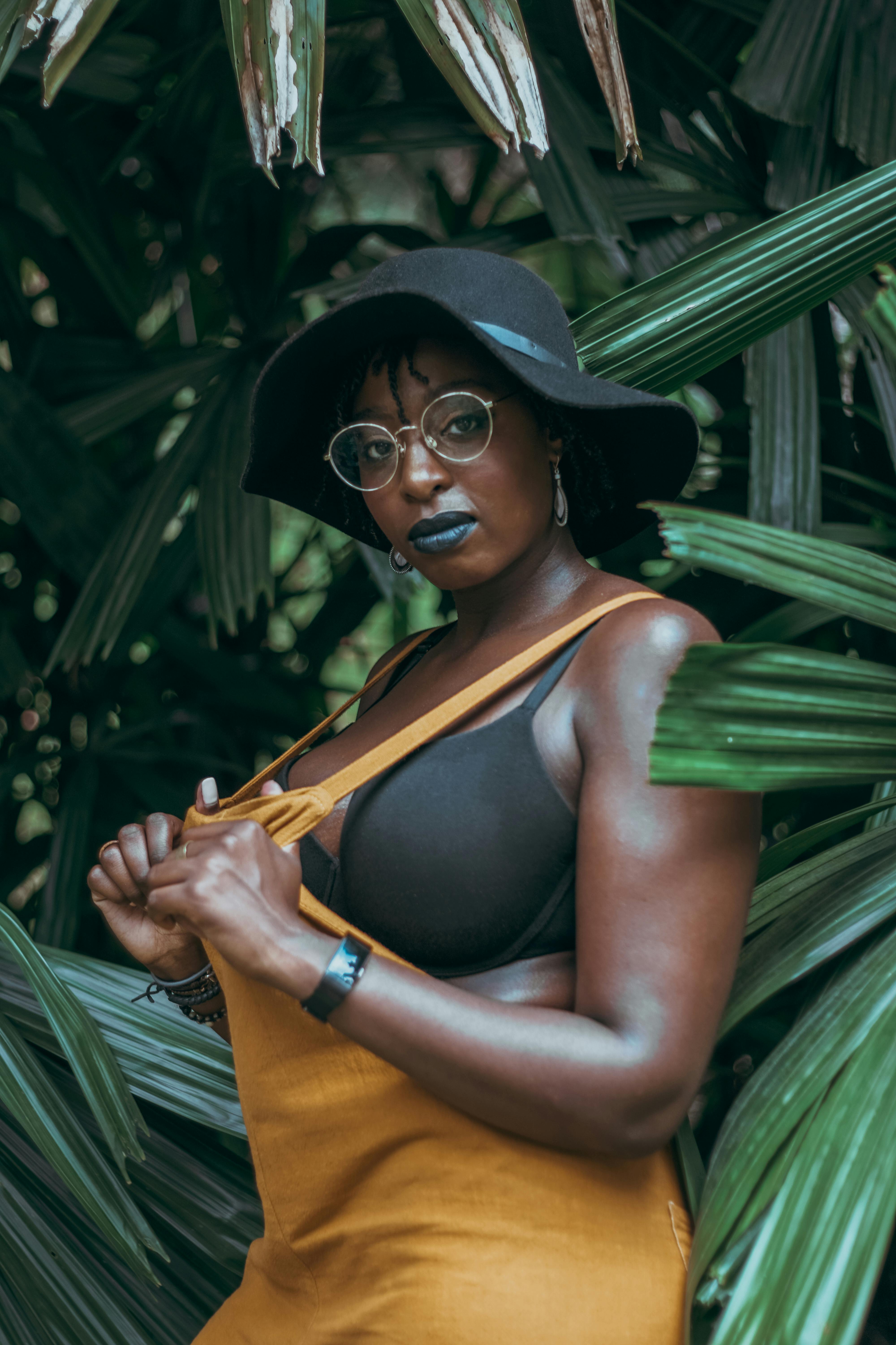 这是一幅优雅的肖像，描绘了一位时尚的非裔美国女性，头戴黑色帽子，置身于郁郁葱葱的热带环境中