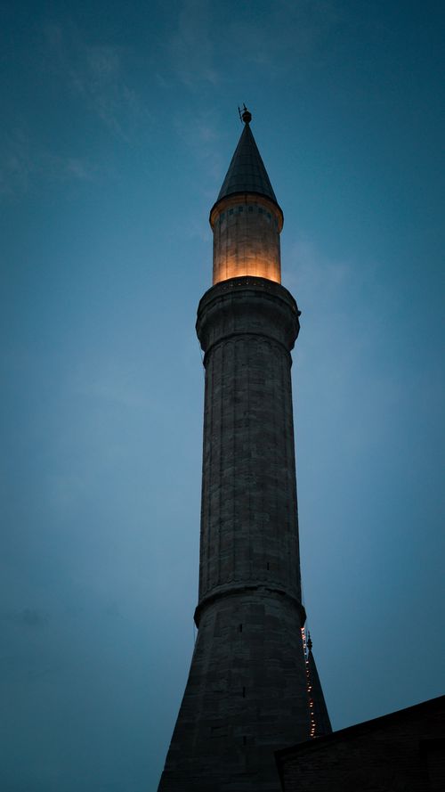 Free A tall, illuminated minaret stands majestically against the twilight sky, showcasing traditional architecture and religious significance. Stock Photo