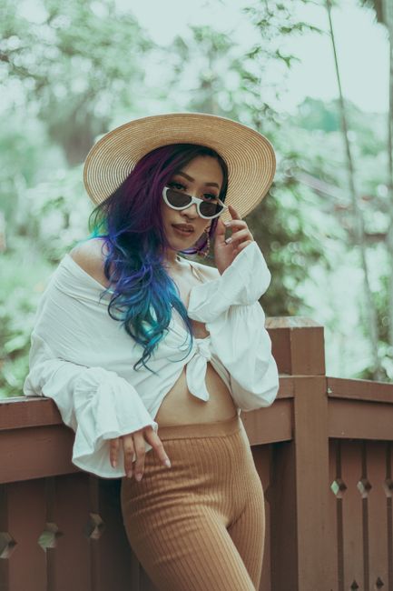 Stylish woman with colorful hair enjoys a sunny day, wearing a sun hat and sunglasses.