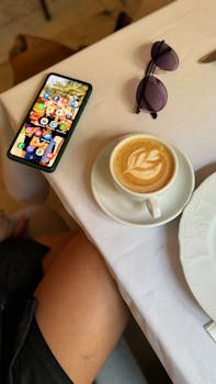 Cozy morning scene with coffee, smartphone, and sunglasses on a table.