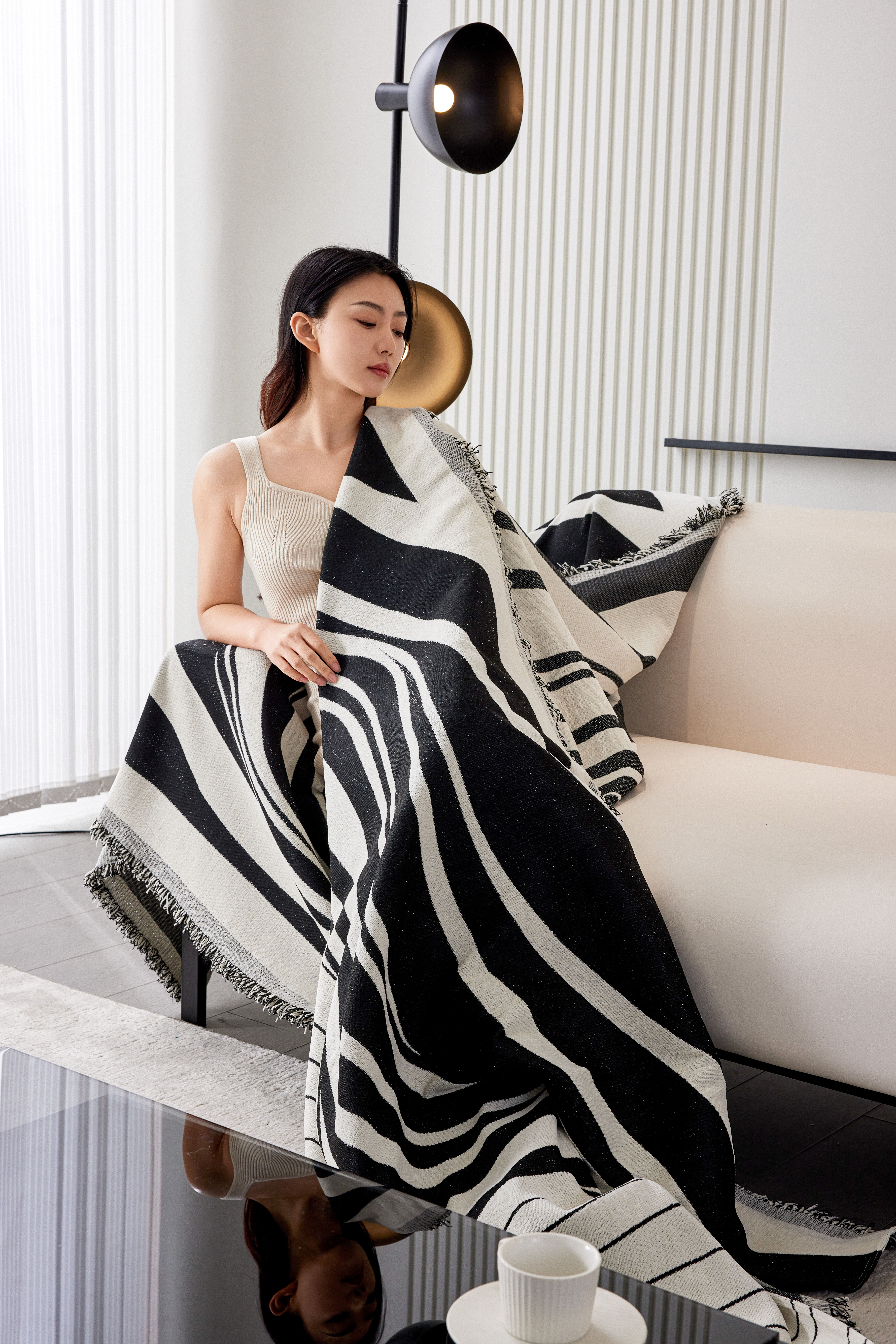 Elegant woman sitting on a sofa wrapped in a chic black and white blanket indoors.