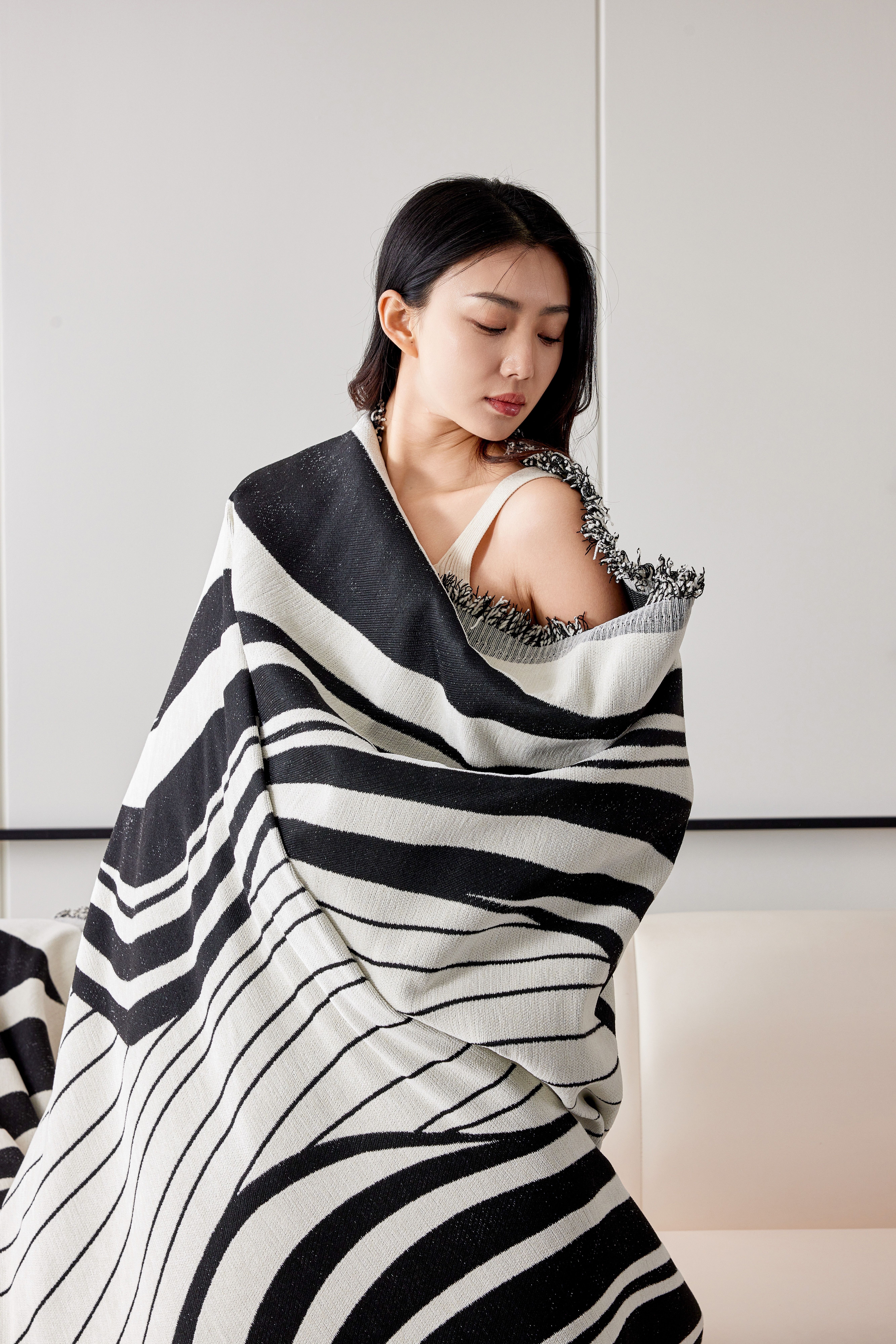 A woman wrapped in a stylish black and white striped throw in a modern living space.