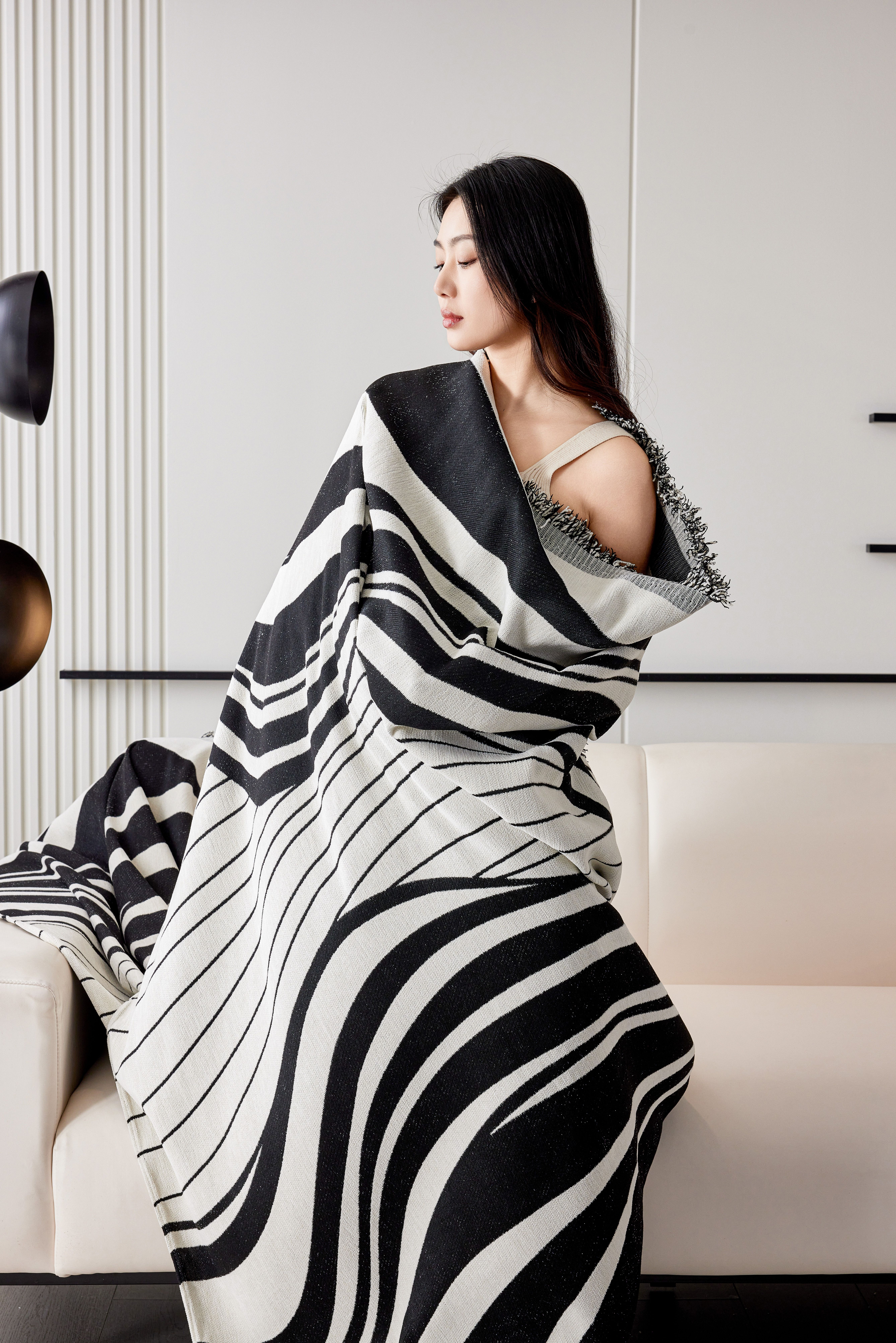 Portrait of a woman elegantly wrapped in a black and white striped blanket, sitting on a modern sofa.