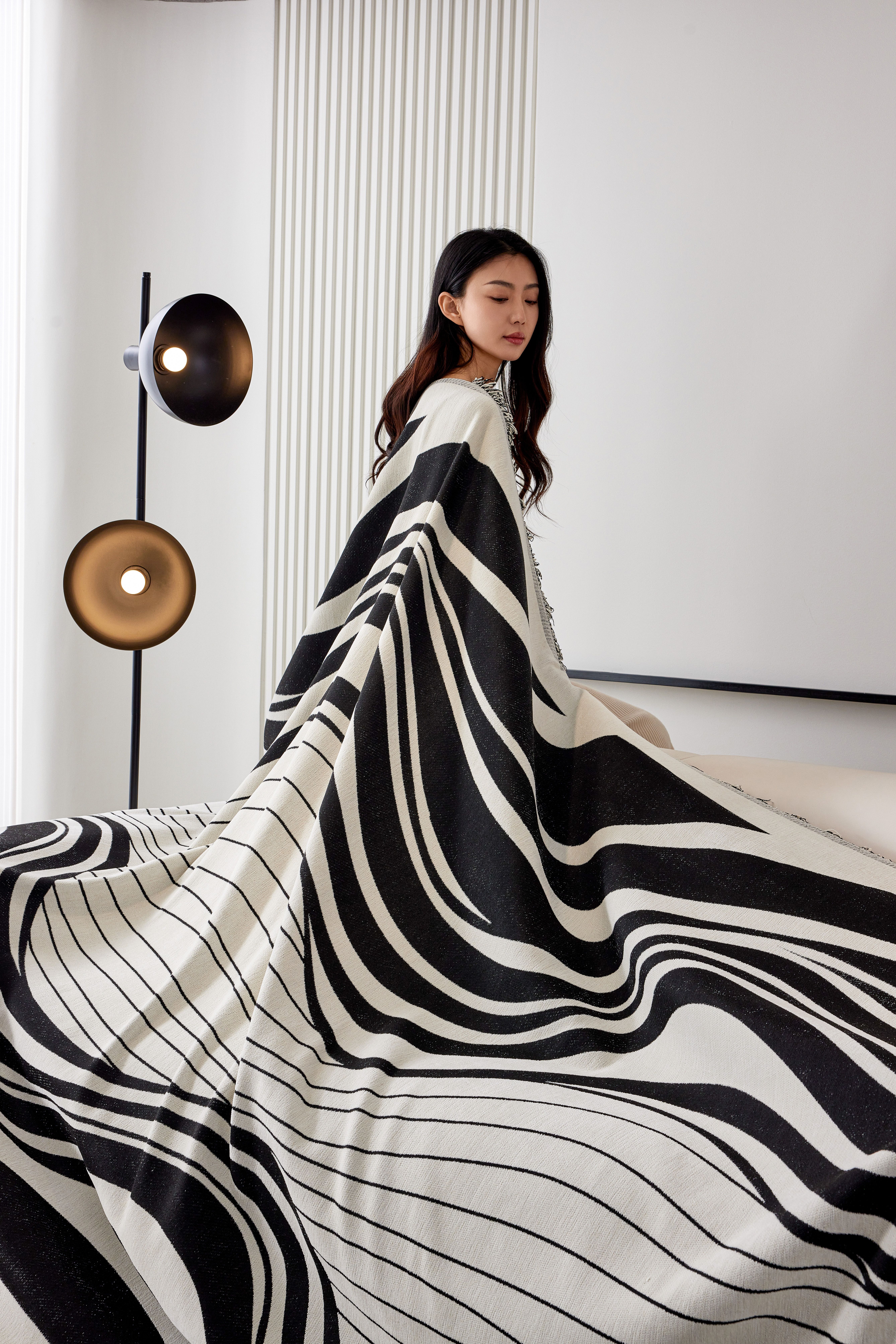 Woman elegantly draped with a stylish black and white blanket in a modern home setting.