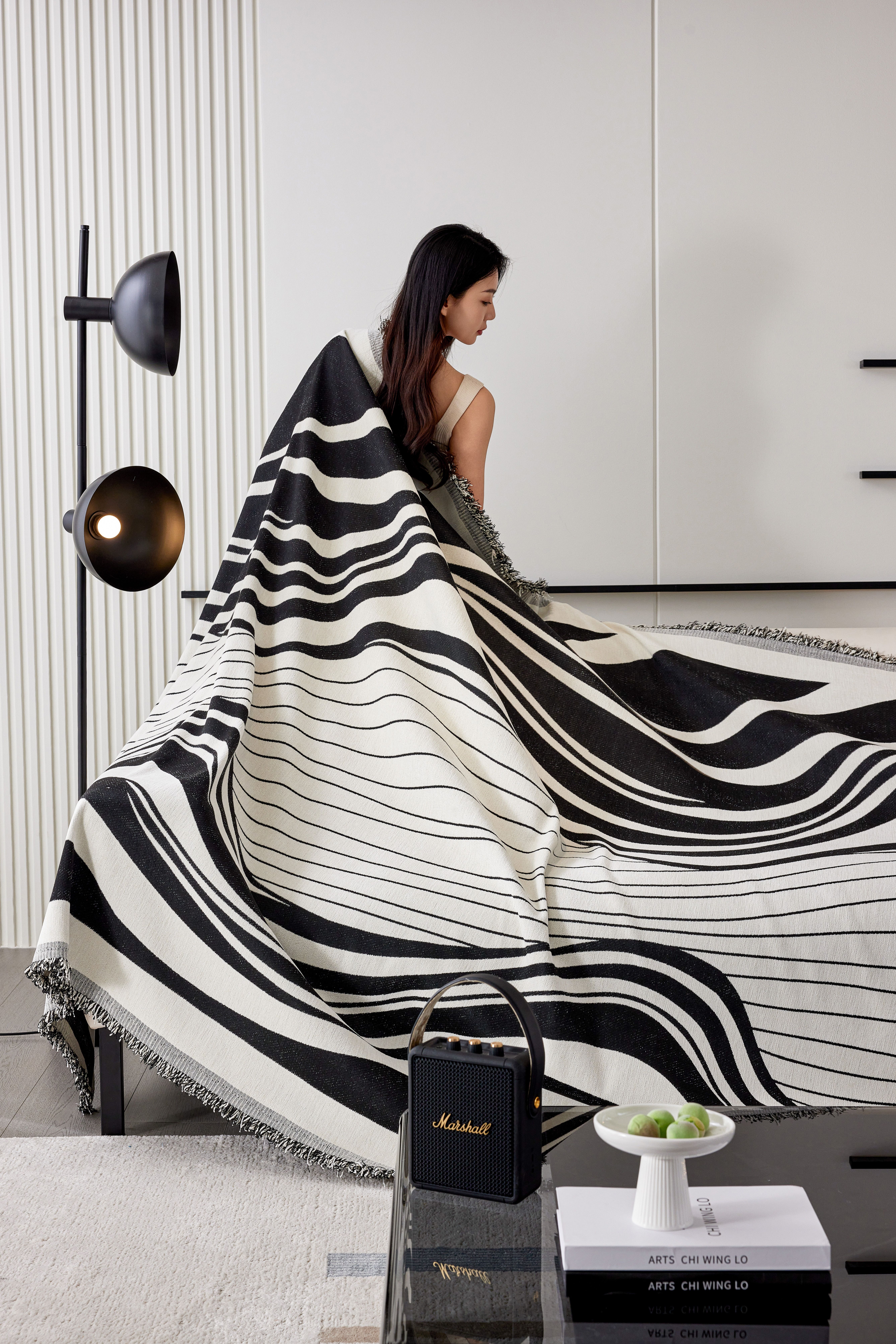Woman elegantly seated with a decorative black and white blanket in a modern living room.