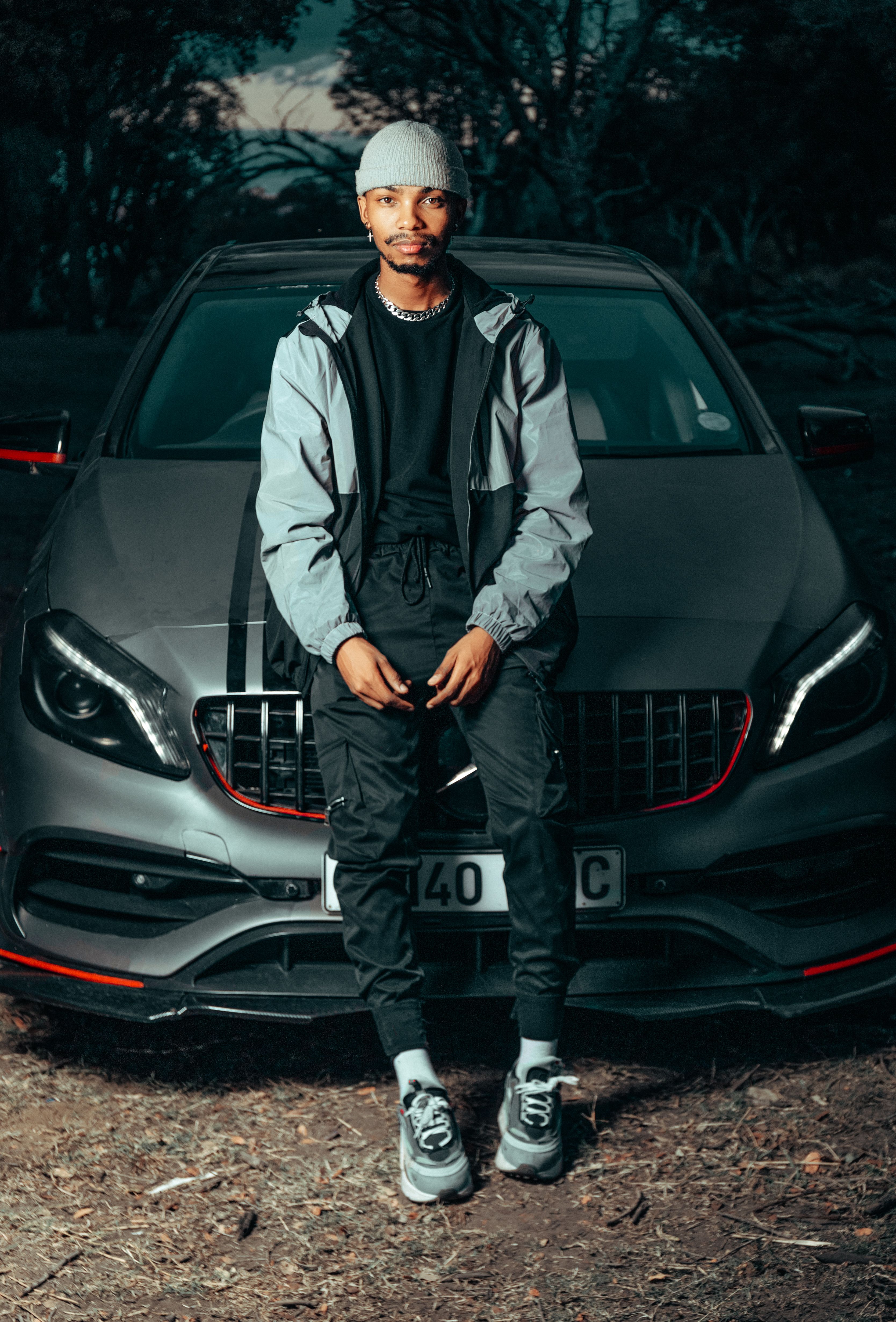 Fashionable young man sitting on a luxury sports car, exuding style and confidence outdoors.