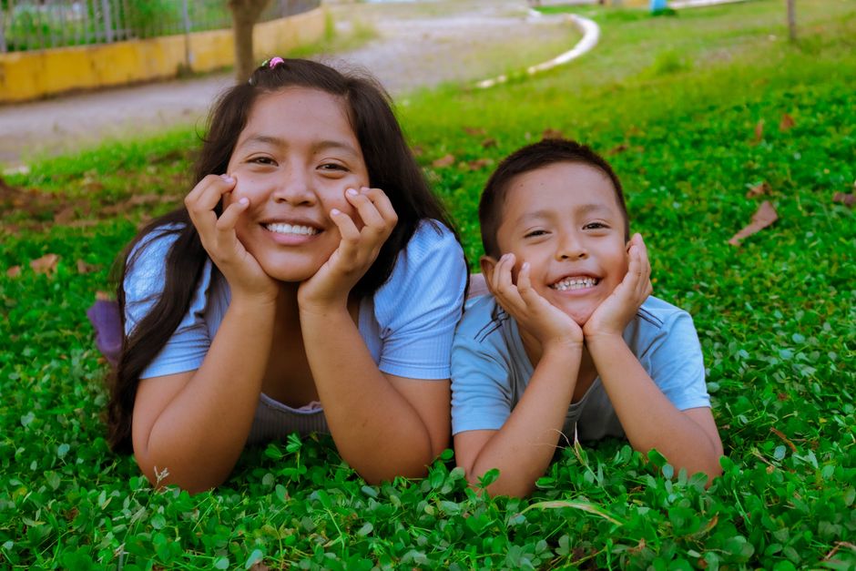 Fotomural Un dúo alegre de un adolescente y un niño tumbados en la hierba, compartiendo sonrisas alegres al aire libre.
