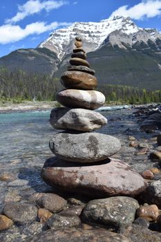 A tranquil stack of stones by a clear river with a majestic mountain backdrop in Banff National Park.