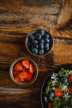 A rustic flat lay of berries and salad on a wooden table, perfect for food themes.