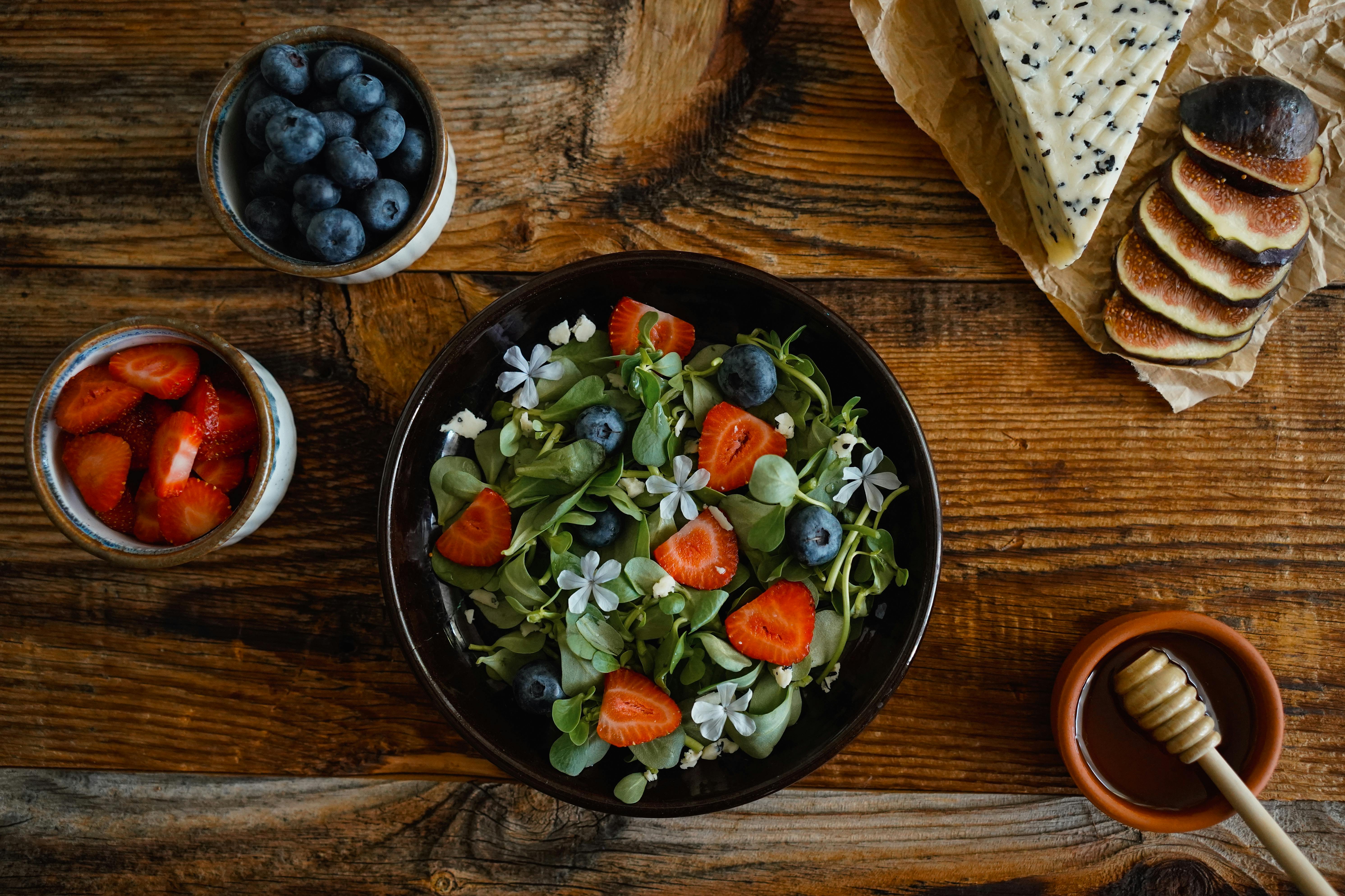 Top view of a fresh, vibrant salad with strawberries, blueberries, and edible flowers on a rustic wooden table.