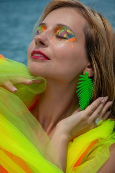 A woman enjoys the summer sun, showcasing vibrant makeup and neon fashion.