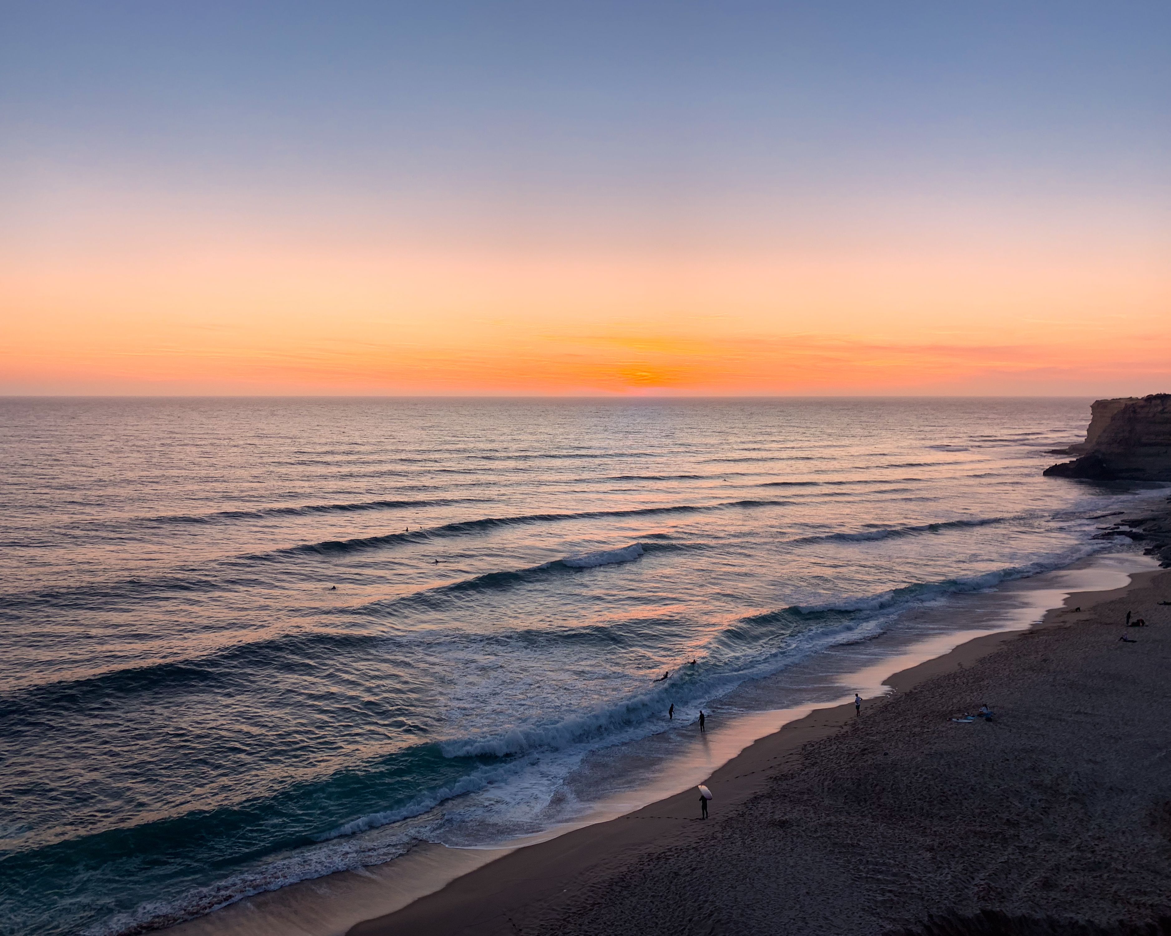 Captivating sunset view over Ericeira Beach, Portugal with gentle waves and sandy shore.