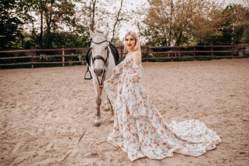 Free A woman in a floral dress poses elegantly with a horse in an outdoor setting. Stock Photo