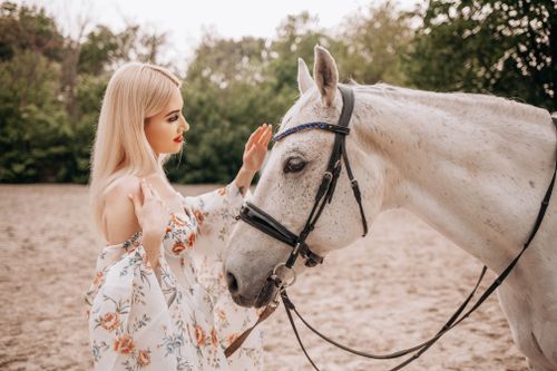 Free A beautiful woman in a floral dress lovingly interacting with a white horse outdoors. Stock Photo