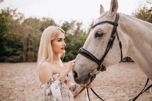 Free A young blonde woman lovingly pets a white horse in an outdoor setting, showcasing a gentle bond. Stock Photo